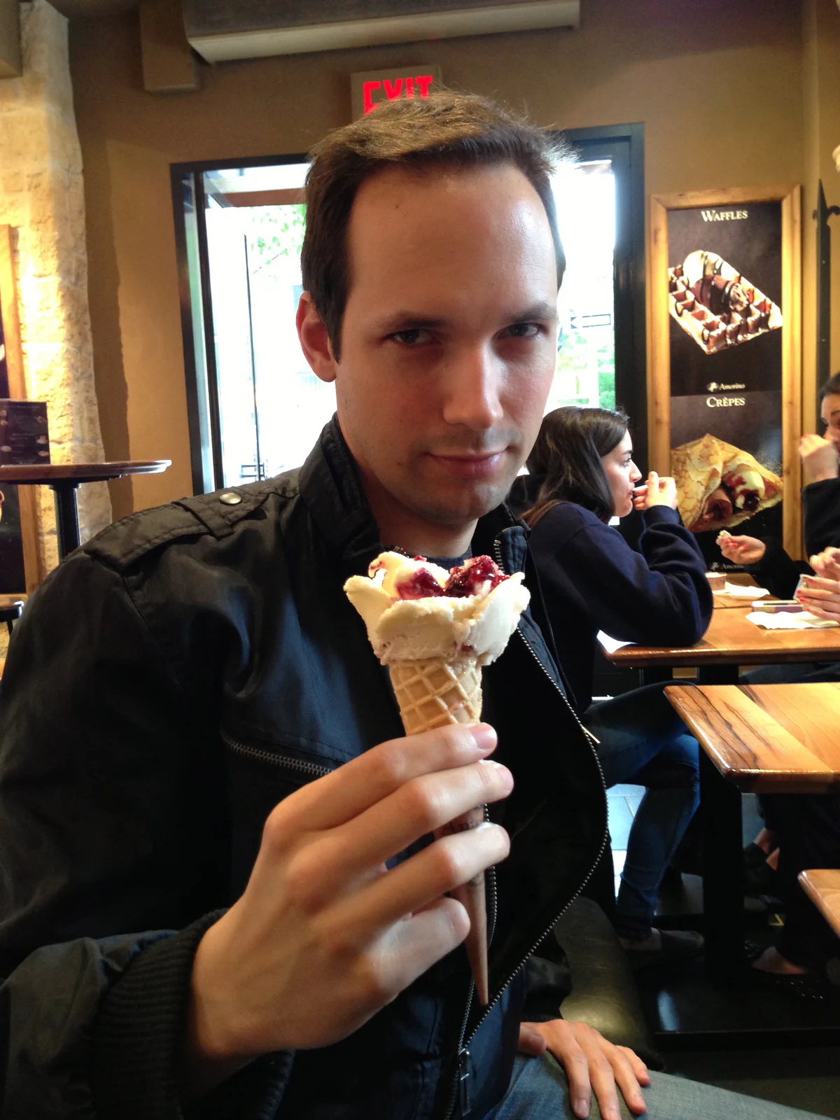 Man in a black jacket holding an ice cream cone in a cafe