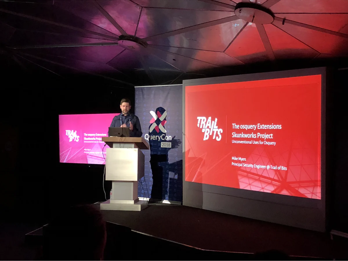 Mike Myers presenting The osquery Extensions Skunkworks Project at QueryCon 2018, with the Trail of Bits logo displayed on the screen behind him
